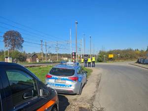 umundurowani policjanci strażnicy ochrony kolei stoją przy otwartym przejeździe kolejowym.