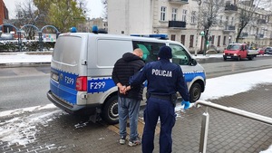 umundurowany policjant stoi z zatrzymanym mężczyzną na tle oznakowanego radiowozu.