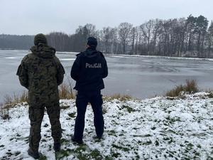 umundurowany policjant wraz z umundurowanym funkcjonariuszem straży rybackiej kontrolują zbiornik wodny.