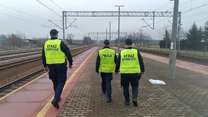 Umundurowany policjant idący wraz z funkcjonariuszami Służby Ochrony Kolei przy torowisku.