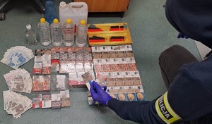 Nieumundurowany policjant z opaską z napisem policja prowadzący czynności z zabezpieczonym alkoholem i papierosami.