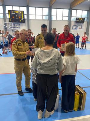 Komendant Państwowej Straży Pożarnej wręcza prezenty zaproszonym gościom.