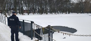 Umundurowany policjant przy zamarzniętym zbiorniku wodnym.