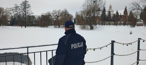 Umundurowany policjant na tle zamarzniętego zbiornika wodnego w Brzezinach.