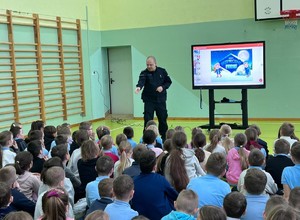 Umundurowany policjant przeprowadza rozmowę z dziećmi.