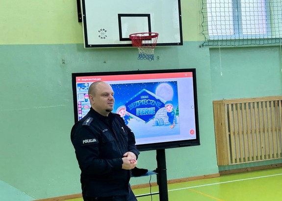 Umundurowany policjant przeprowadzający rozmowę z dziećmi w Szkole Podstawowej nr. 1 w Brzezinach.