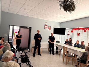 Umundurowani policjanci wraz z kierownikiem placówki podczas spotkania z seniorami.