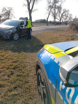 Policjant na tle radiowozu oznakowanego w trakcie kontroli drogowej.
