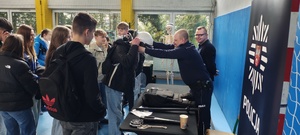 Policjant pomaga w przymierzaniu policyjnego wyposażenia.