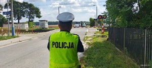 Umundurowany policjant Wydziału Ruchu Drogowego przeprowadza kontrolę przejazdu kolejowego.