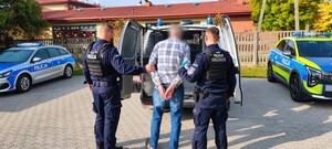Umundurowani funkcjonariusze nadzorują osobę zatrzymaną.