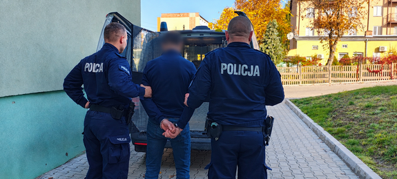 Umundurowani funkcjonariusze nadzorują osobę zatrzymaną.