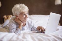starsza pani leżąca na łóżku z laptopem